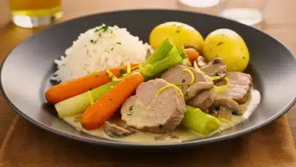Assiette de blanquette de veau au citron servie avec carottes, poireaux, champignons, riz et pommes de terre.