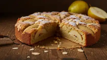 Gâteau moelleux aux poires et aux amandes, saupoudré de sucre glace et de lamelles d’amandes, présenté sur une table en bois rustique.