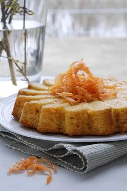 Gâteau aux carottes doré et moelleux, décoré de fines lamelles de carottes sur une assiette blanche, posé sur une nappe en lin.