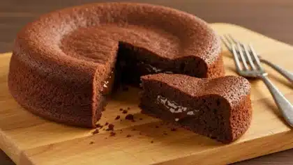 Fondant au chocolat découpé, laissant apparaître un cœur coulant brillant sur une planche en bois.