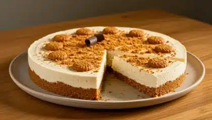 Cheesecake sans cuisson avec base de spéculoos et mousse crémeuse, décoré de biscuits et présenté avec une part déjà découpée.