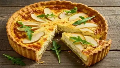 Quiche au fromage garnie de tranches de poire et de roquette sur une pâte dorée, avec une part découpée posée en avant.