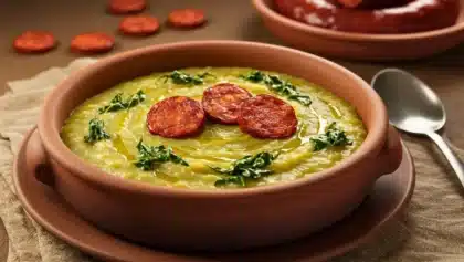 Bol de caldo verde portugais garni de fines tranches de chorizo et de chou kale, servi chaud dans une assiette en terre cuite.