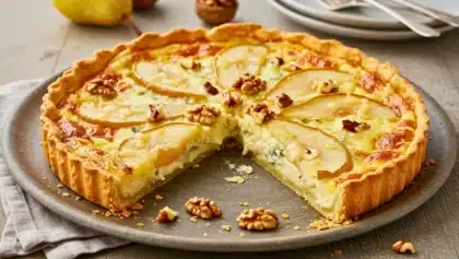 Tarte poires et Roquefort garnie de cerneaux de noix, entamée pour montrer la garniture crémeuse au fromage et les lamelles de poire fondantes sur le dessus.