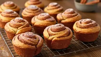 Cruffins maison dorés et saupoudrés de sucre glace, disposés sur une grille de refroidissement avec un fond en bois chaleureux.