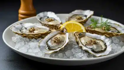 Assiette d’huîtres ouvertes posées sur de la glace, garnies de poivre fraîchement moulu et accompagnées d’un quartier de citron, décor festif en arrière-plan.